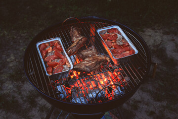 Grilled meat on charcoal close-up. Aluminum containers with cutlets and vegetables. Red-and-yellow...