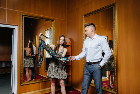 A Young Couple Tries On New Clothes In The Fitting Room Of A Store, Shopping In A Supermarket.