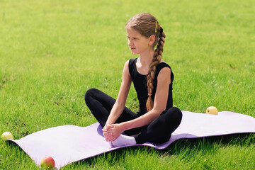 slim girl in a black gymnastic uniform performs gymnastic exercises or pilates on the green grass in the park. Professional gymnast during training	
