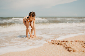 Fototapeta premium Six year girl in yellow swimsuit on the beach. hot summer day.