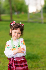 Portrait of a joyful young girl in Ukrainian national clothes on a green background. Outdoors. Happy smile. Hands outstretched for a hug.	