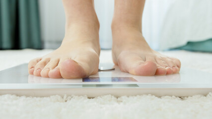 Young barefoot woman standing on digital scales to measure her weight. Concept of dieting, loosing...