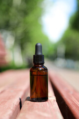 Obraz na płótnie Canvas Skincare brown glass bottle with dropper on wooden bench. Photo with selective focus on natural green blurred background
