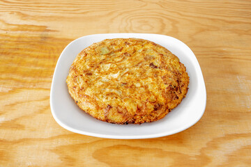 Popular Spanish cooking recipe for Spanish omelette on white plate and pine wood table