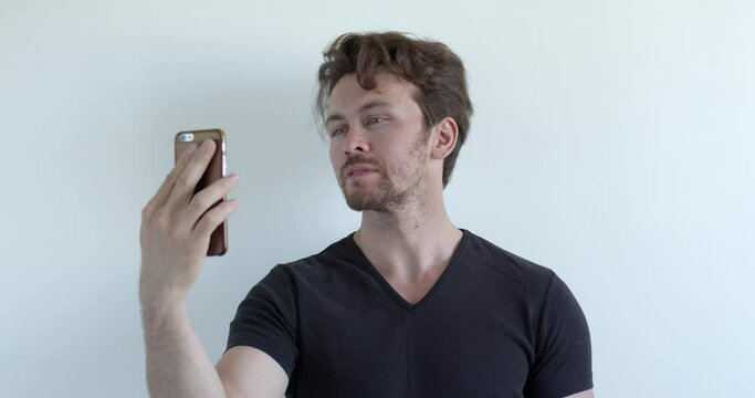 young man making selfie photo on smartphone, looking at camera posing, side view. adult male in black t-shirt use modern technologies. copy space for advertisement. media, people lifestyle concept