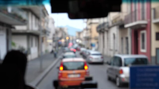 Looking through city bus front window or windshield. Blurred view of slow traffic in Italian town street in the evening.
