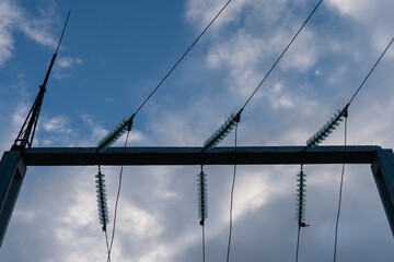 A close-up shot of high-voltage transmission lines with insulators suspended from a steel tower, set against a moody, cloudy sky. Energy infrastructure and power distribution system. 