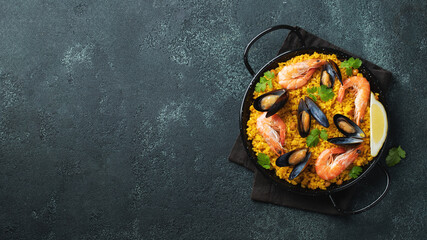 Traditional spanish seafood paella in pan with chickpeas, shrimps, mussels, squid on black concrete background. Top view with copy space