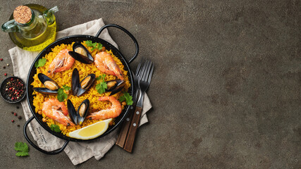 Traditional spanish seafood paella in pan with chickpeas, shrimps, mussels, squid on brown concrete background. Top view with copy space