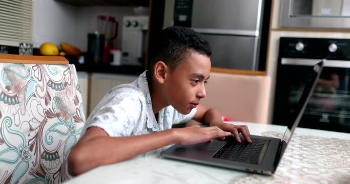 Black kid in front of laptop at home. Child browsing internet online computer