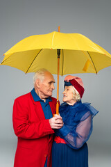 elderly man in red blazer and woman in blue dress and turban holding yellow umbrella isolated on...