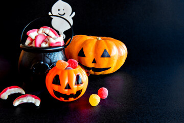 Happy Halloween decoration on black background. Pumpkin with colored candies, ghost and cauldron.