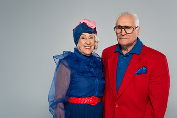 smiling elderly couple in stylish clothes looking at camera isolated on grey