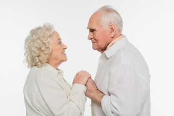 happy elderly couple gently holding hands and looking at each other isolated on white