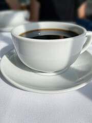 Close up of coffee in white cup and saucer on white linen tablecloth