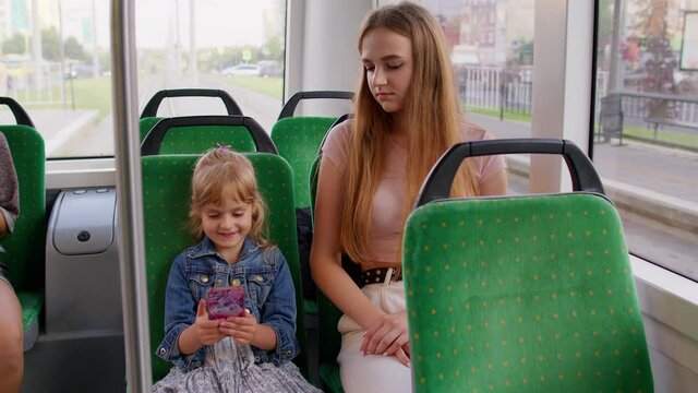 Tired sleepy woman with daughter traveling by bus going home after hard work day. Mother sleeping while little child kid girl play on smartphone. Family passengers rides public tram or train transport