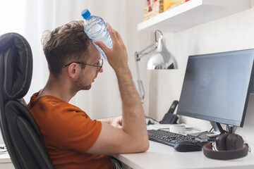 Working at home man suffering from heat and thirst cools down with water bottle at hot summer day