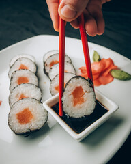 Plato de sushi de salmón con un poco de salsa de soja y de jengibre, una mano que sostiene los palillos chinos