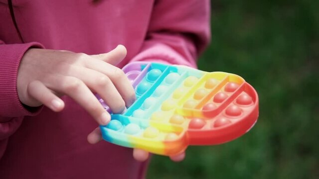 Close up bunner shot of hands unrecognizable kid holding rainbow Pop It fidget toy in hands. Teen Playing, Push soft silicone bubble. Popular trend 2021. anti stress toy. slow motion. 