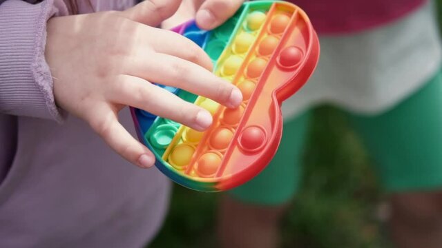 Close up bunner shot of hands unrecognizable kid holding rainbow Pop It fidget toy in hands. Teen Playing, Push soft silicone bubble. Popular trend 2021. anti stress toy. slow motion. 