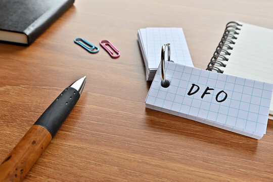 There is a word book with the word of DFO which is an abbreviation for Data Feed Optimization on the desk with paper clips, a pen and notebook.