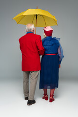 back view of senior couple in stylish clothes walking with yellow umbrella on grey