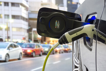 Power supply connect to electric car for add charge to the battery. Charging re technology industry transport which are the future of the Automobile with city background.	