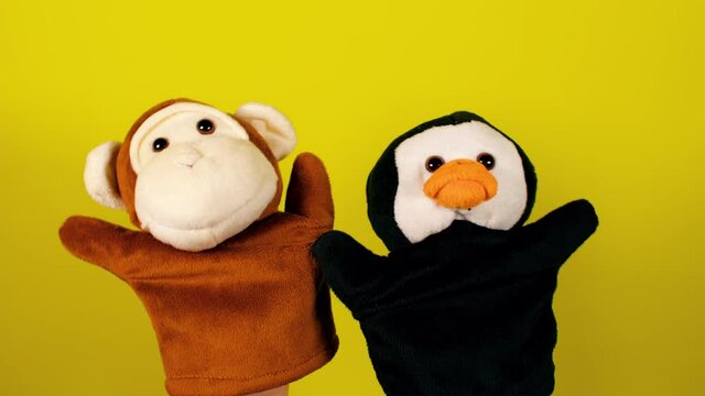 Soft puppet toys on hands on yellow background. Concept of puppet show. Close-up of hands with puppet monkey and penguin.
