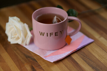 Wifey's tea cup and white rose on colorful napkin resting on wooden table (further away)