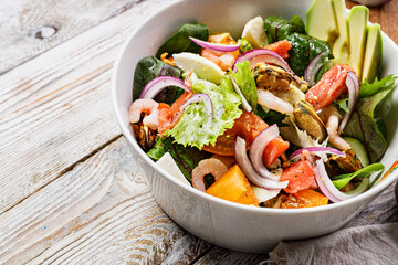 Close-up delicious summer Mediterranean salad. Mussels, shrimp, salmon, tomatoes, ice salad, avocado, red onion, Swiss chard, spices, and olive oil. Seafood salad on a rustic background. Copy space