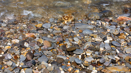 Top view of sea rocks or granite pebbles while getting light waves making white bubbles and light reflection. Background of wet stone at sea shore