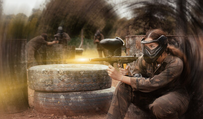 Portrait of girl paintball player in mask who is aiming in opponents on paintball field