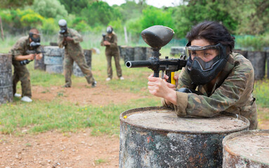 Asian female paintball player in protective mask and with gun on paintball field