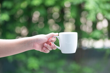 Woman left hand holding coffee mug, natural background