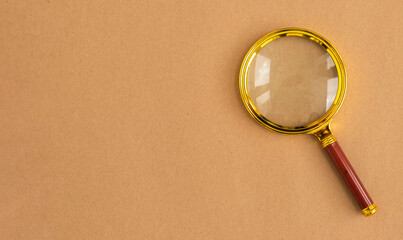 Golden magnifying glass over brown carton background. Search tool with copyspace.