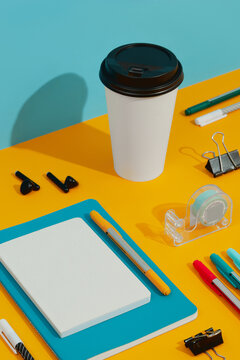 Colorful notepads, pens and paper cup on orange table