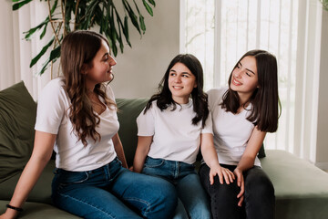 Three pretty smiling caucasian girls in white shirt sitting on the green sofa