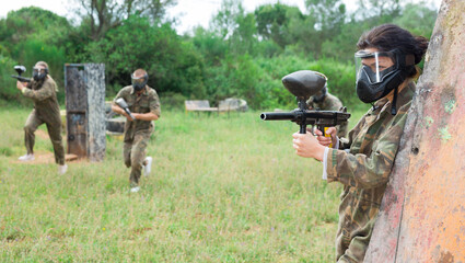 Group of friends paintball players of opposite teams in shootout in forest outdoors