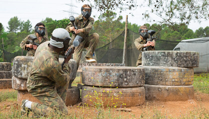 Group of friends paintball players of opposite teams in shootout in forest outdoors