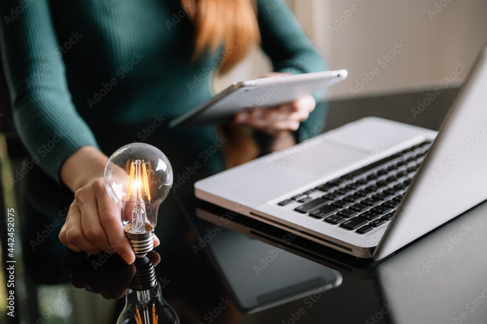 Poster business hand holding lightbulb with using laptop computer and money stack in office. idea saving en