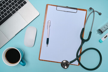 Clipboard, laptop computer, stethoscope, and coffee cup on doctor workspace.