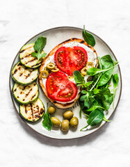 Sandwich with whipped ricotta, tomatoes, olives and grilled zucchini - delicious snack, tapas on a light background, top view