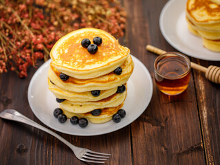 Sweet food. Stack of delicious pancakes with blueberries, Strawberry and Strawberry jam, fork rests in white plate on blur wooden background.