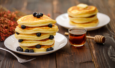 Sweet food. Stack of delicious pancakes with blueberries, Strawberry and Strawberry jam, fork rests in white plate on blur wooden background.