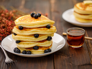 Sweet food. Stack of delicious pancakes with blueberries, Strawberry and Strawberry jam, fork rests in white plate on blur wooden background.
