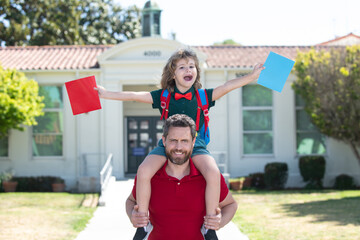 Excited father piggyback ride son to school. Parent and pupil of primary school schoolboy with...