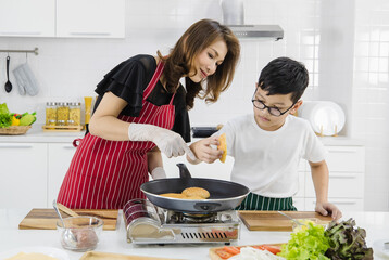 Asian woman and boy putting fresh buns on hot pan while cooking burgers for lunch in kitchen at home. Conept for love and relationship time shairing in modern family