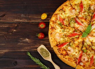 Close up on homemade seafood pizza with shrimp, crab sticks, bell peppers topping on wooden plate,...