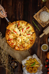 Selective focus and close up piece of pizza on spatula or scoop by hand holding or presenting with blur of wooden background and decorated by sackcloth, ingredients, fried potatoes and cold beverage.