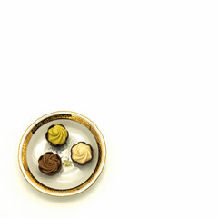 On the saucer are three chocolates with a cream filling. On the plate there is a floral ornament and a gold border. View from above. Bottom left corner. Isolated on white background